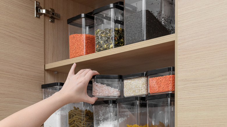 A person's hand reaching for a container of spices in a kitchen cabinet
