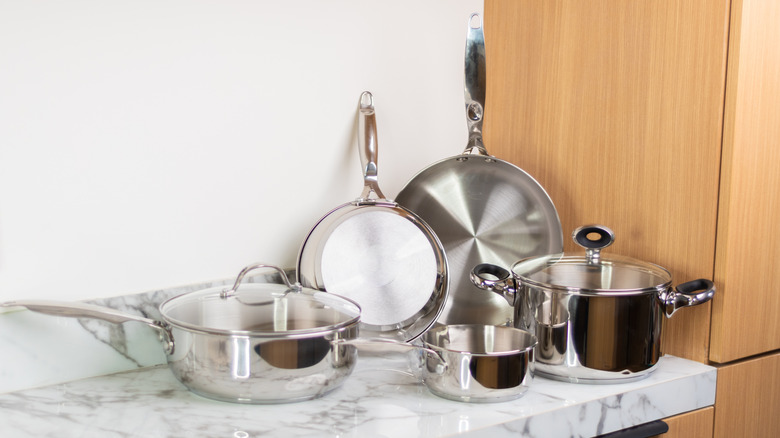 A set of stainless steel pots and pans on a marble countertop