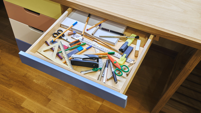 a messy desk drawer cluttered with office supplies