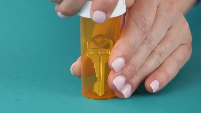 Woman tucking housekey into empty orange prescription bottle with sealed lid