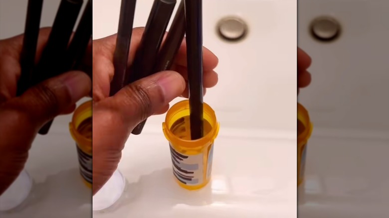 Woman dropping eyeliner makeup pens into pill bottle with redacted label