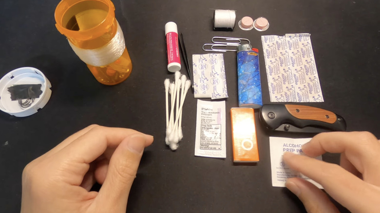 Empty pill bottle and various essentials scattered around it on black table