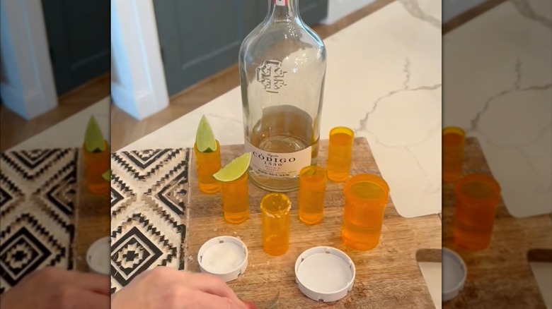 Empty orange pill bottles used as shot glasses on wood platter with liquor bottle