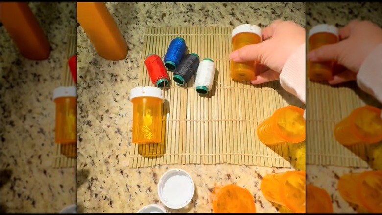 Woman tucking thread spools into empty pill bottles on sushi mat on counter
