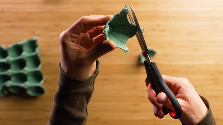 Hands using scissors to cut cups out of green paper egg carton over wood table