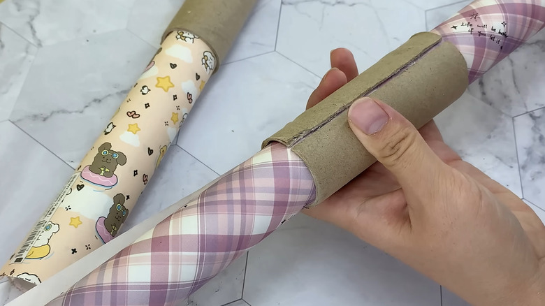 A person securing cute wrapping paper with toilet paper rolls above tile surface