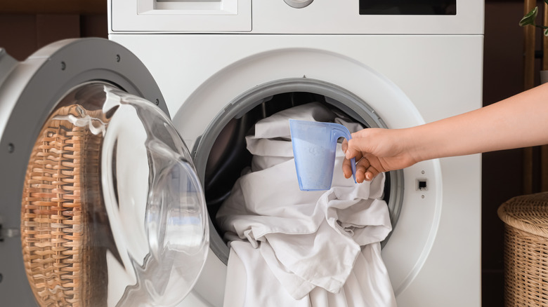 a woman holds laundry detergent next to an open washing machine