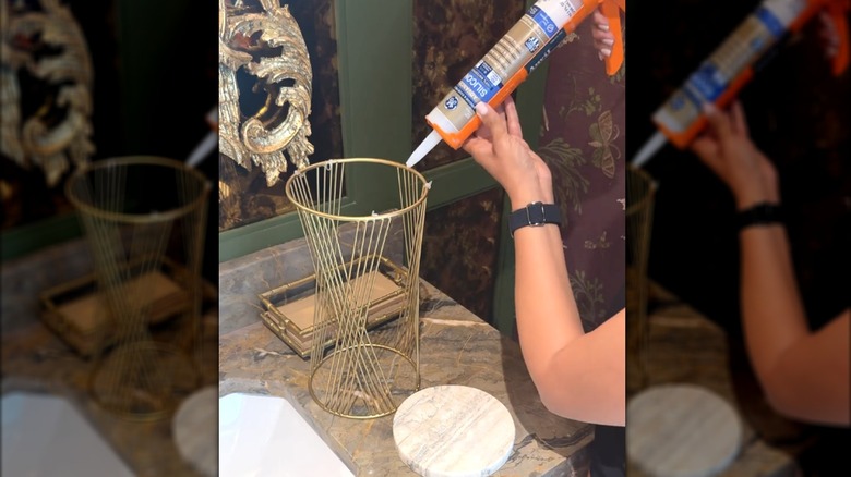 Woman using silicone glue to craft marble and gold toilet paper holder on a stylish stone bathroom countertop