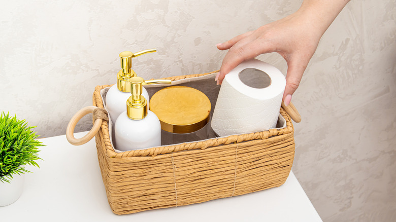 Person putting a roll of toilet paper into a basket on a counter