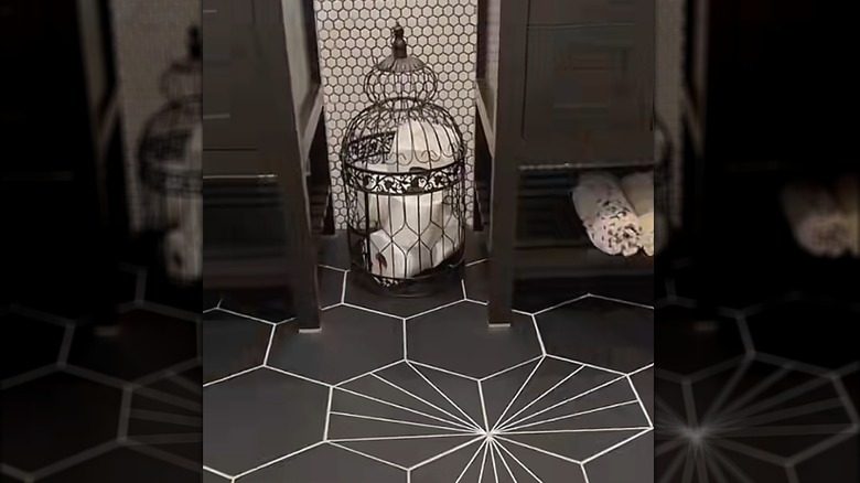 Bird cage sitting on the floor of a bathroom with toilet paper inside