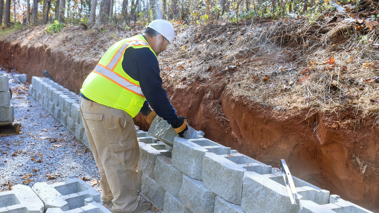 A construction worker is using concrete blocks to build a retaining wall