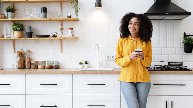 Woman holding a phone while standing in front of an organized countertop