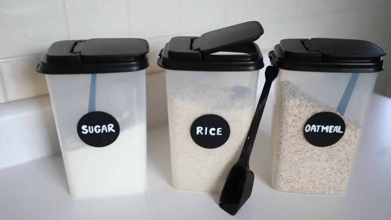 Sugar, rice, and oatmeal are stored in tall plastic containers on a kitchen countertop