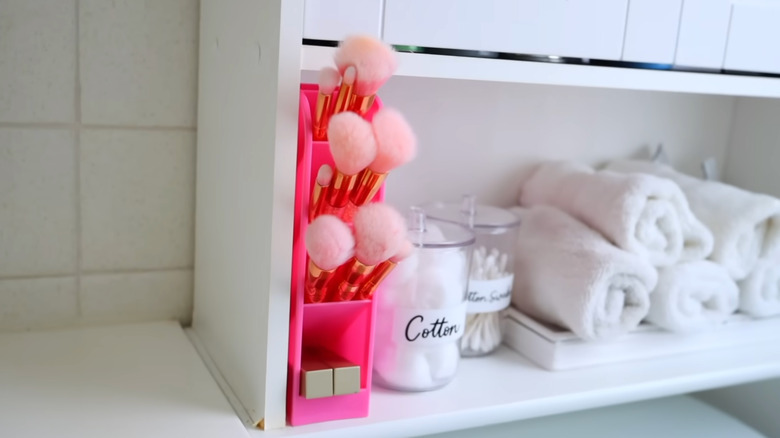 Assorted makeup brushes are organized in a pink pencil container on a bathroom counter