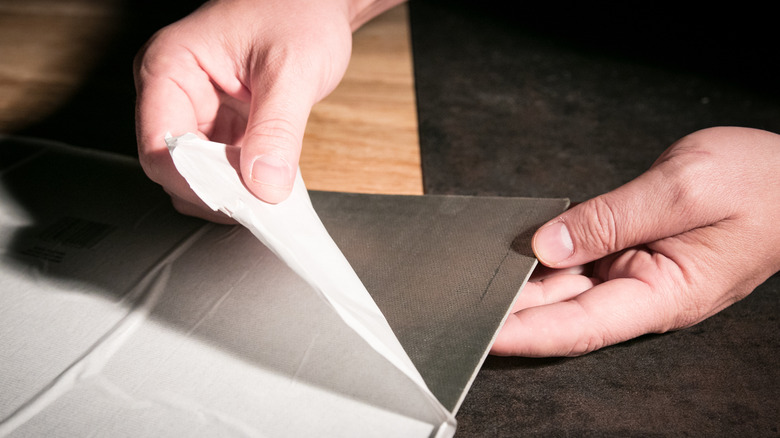 Person peeling an adhesive floor tile