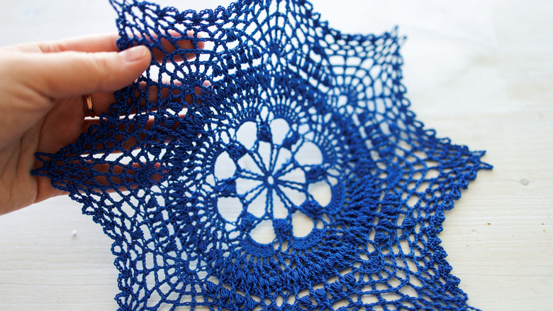 A person holds a bright blue doily