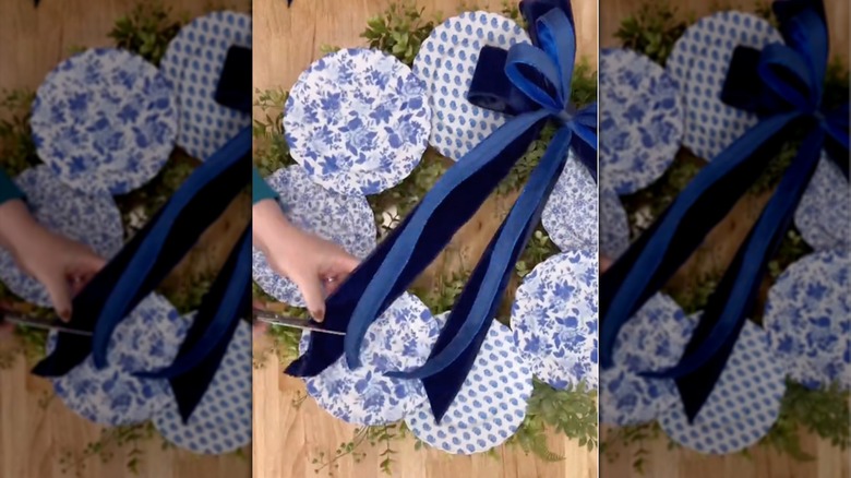 Woman cuts ribbon on handmade wreath made of plates covered in napkins