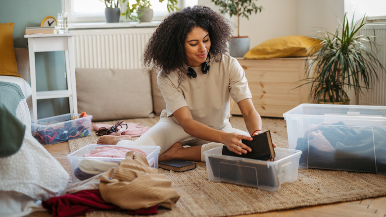 A woman sits on the floor while sorting through various items