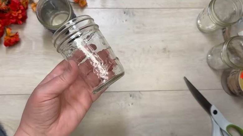 Person holding a Mason jar over a work surface with other mason jars and a pair of scissors in the background