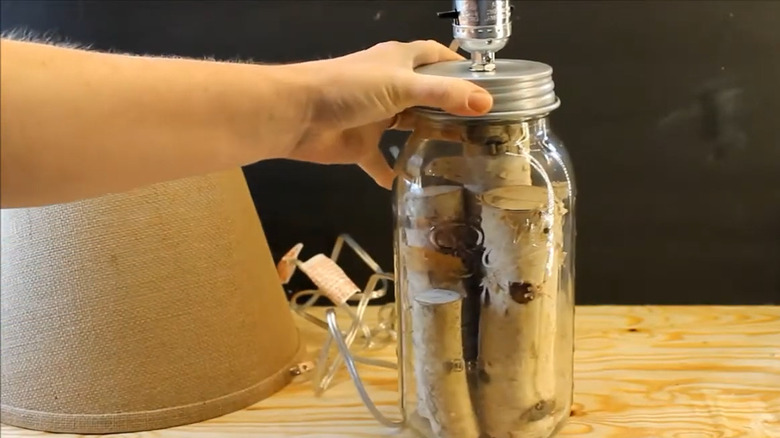 Person assembling a Mason jar lamp with mini logs inside