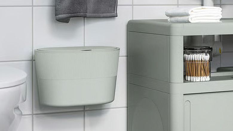 A seafoam green self-adhesive KINNASJÖ Trash can hangs on a tiled bathroom wall