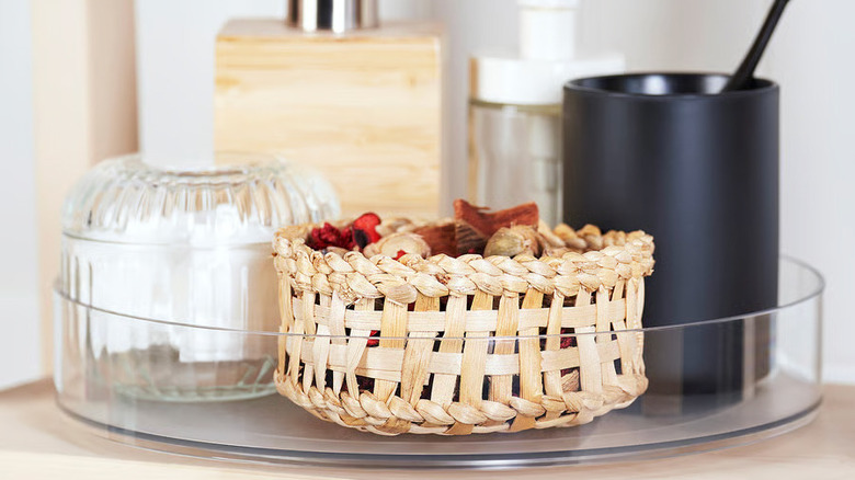 A wicker basket of potpourri and jars full of personal care products sit in a clear KLIPPKAKTUS Lazy Susan