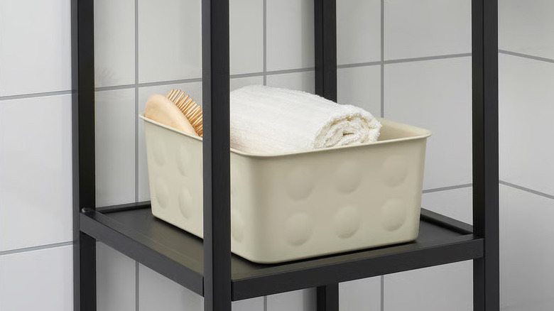 A cream-colored NOJIG Organizer bin sits on a black bathroom shelf
