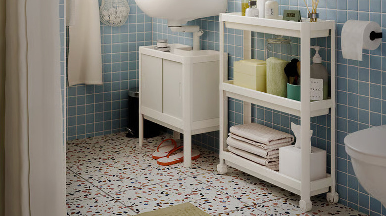 A white VESKEN Cart full of folded towels and bath products sits next to the sink in a colorful bathroom