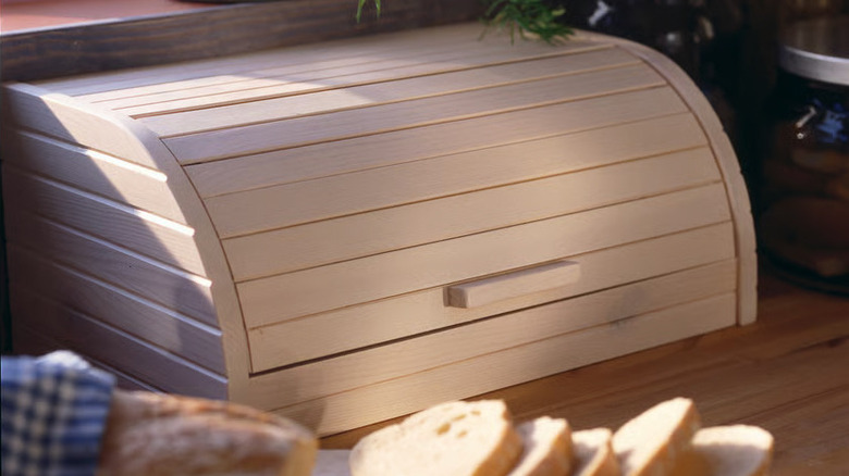 A wooden IKEA MAGASIN Bread bin on a wooden countertop near a sliced loaf of bread