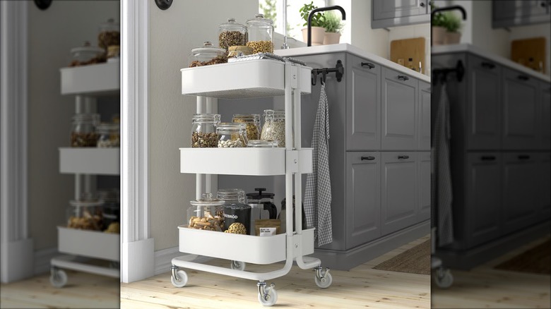 A white IKEA RÅSKOG Utility cart full of glass jars next to gray kitchen cabinets