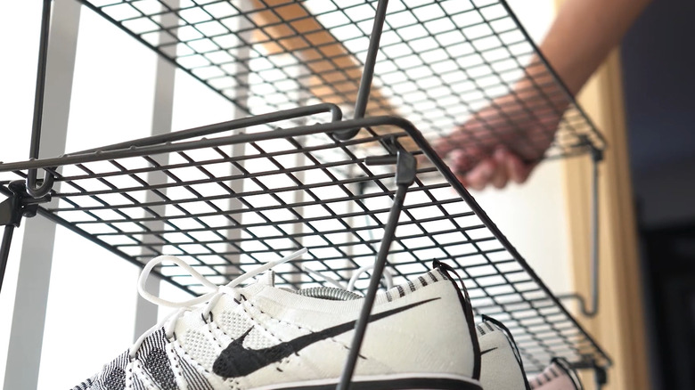 Person putting one level of a metal wire shoe rack on top of another.