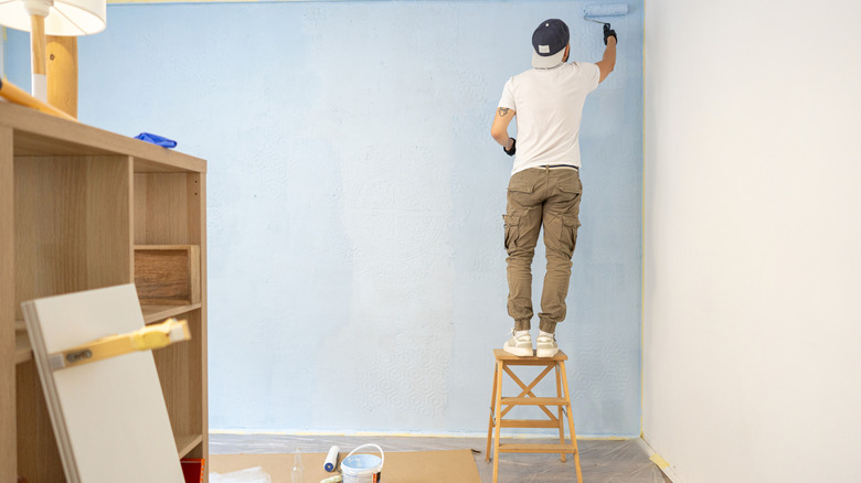 Someone standing on a small step ladder and painting a wall pale blue