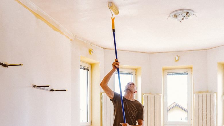 A person painting a living room ceiling using a roller