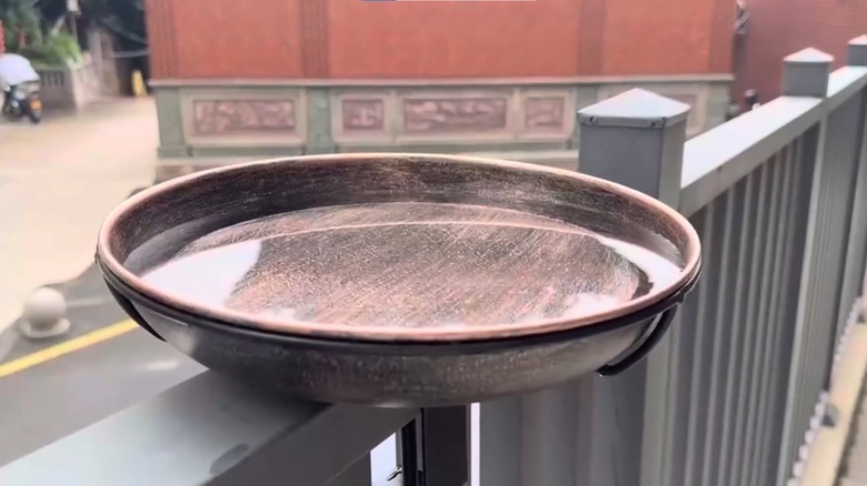 A copper bird bath from OUISJYER mounted to a deck railing and filled with water.