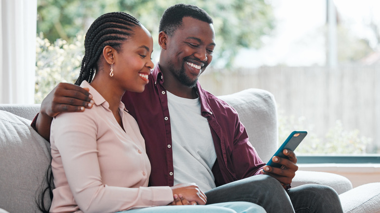 A couple looks at a phone while smiling in a living room