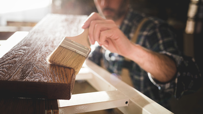 Craftsman applies varnish to solid wood furniture piece