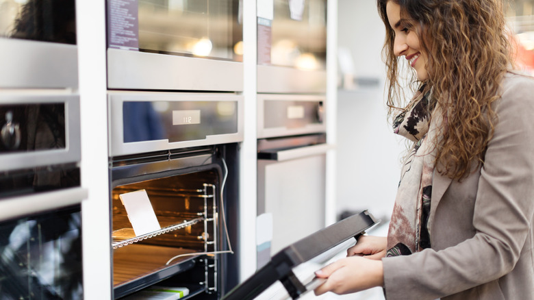 woman shopping for appliances and opening a wall oven