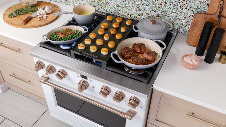 cooking dinner on a white Cafe Appliances stove with gold knobs and handle