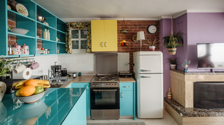 A retro 80's kitchen with a variety of bright colors, a round fridge, and decorative elements