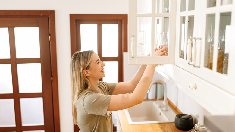 A woman grabs a class from a kitchen cabinet