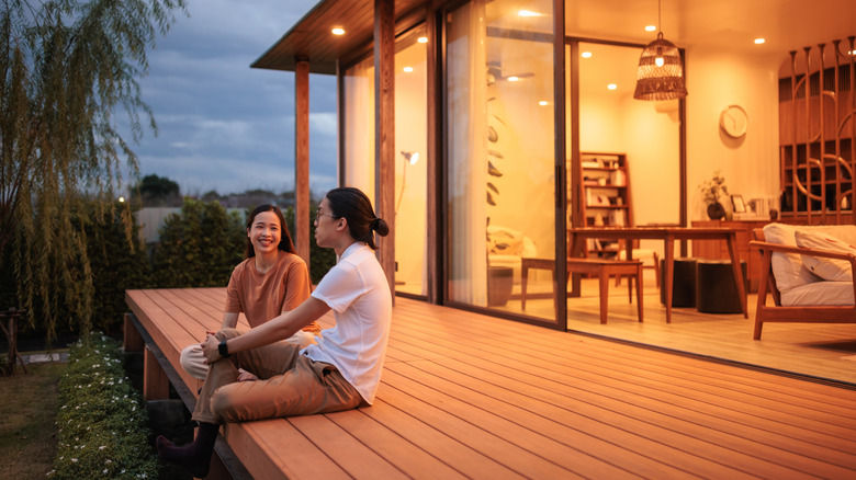 A smiling couple sits on a porch at dusk