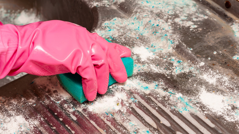 scrubbing oven rack with sponge and cleaning powder