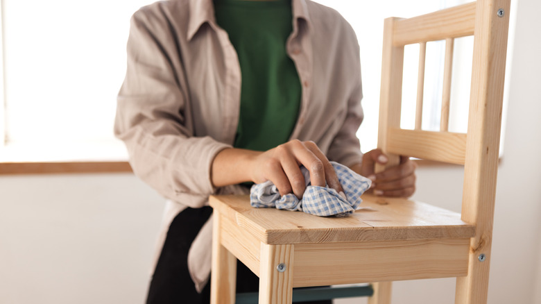 Person wiping down a wooden chair with a light-colored finish