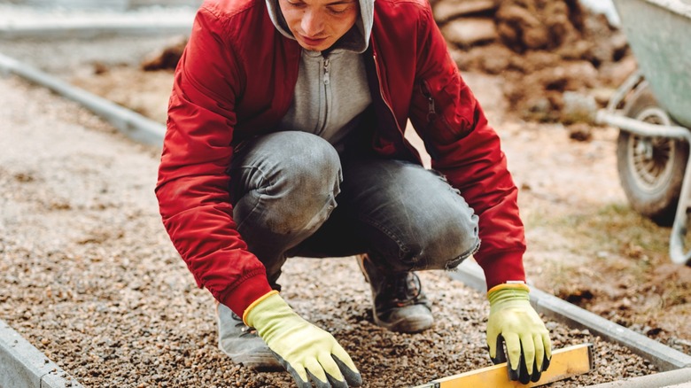 Worker with hoodie leveling gravel with wheelbarrow in the background