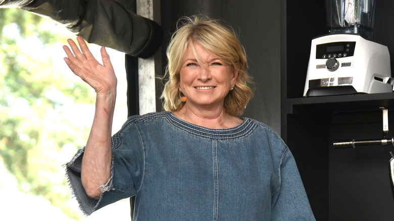 Martha Stewart smiling and waving by cocktail blenders in a kitchen