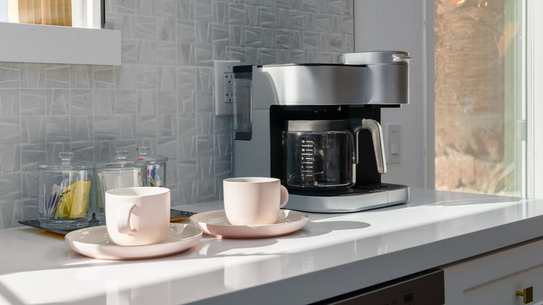 Two white coffee mugs beside coffee maker on kitchen countertop