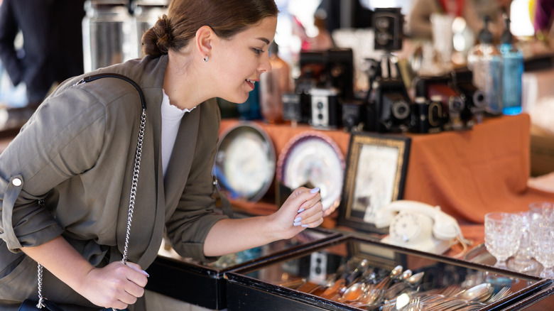 Young female shopper looking at antique silverware