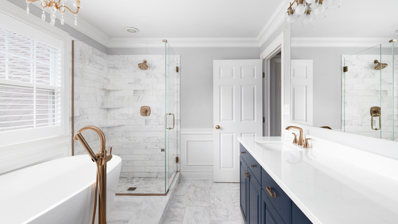 an elegant primarily white bathroom with blue vanity and marble style tile