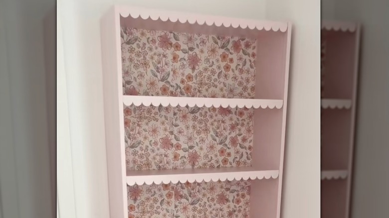IKEA BILLY bookshelf painted pink with scallop trim on each shelf and a floral wallpaper in the inside