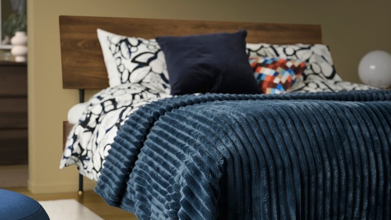 A deep blue blanket lays on the foot of a modern bed